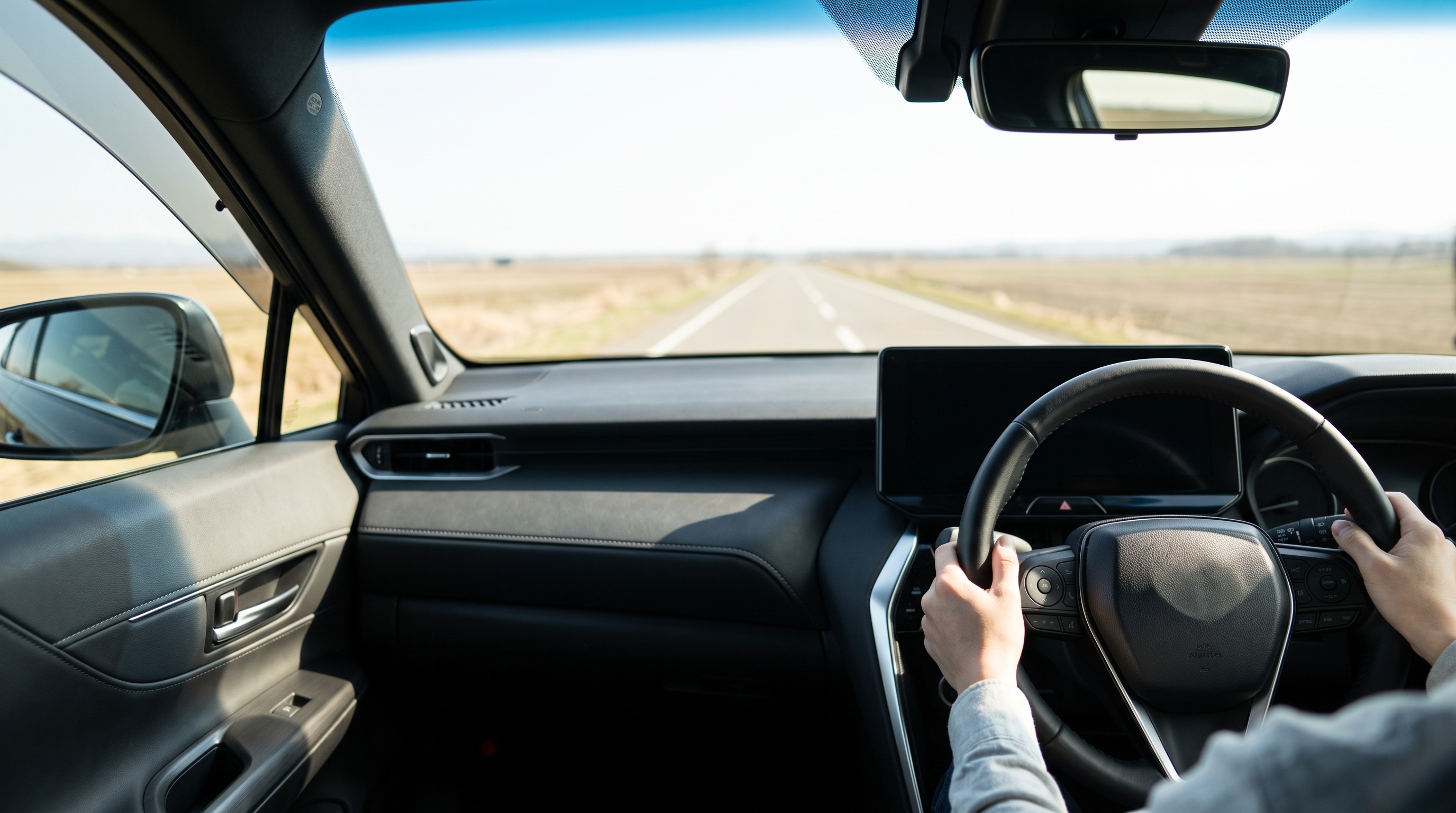 明るい日差しが差し込むSUVの運転席で、ステアリングやセンターコンソールの質感を確認しているクローズアップショット。窓越しには広々とした直線道路が見える。