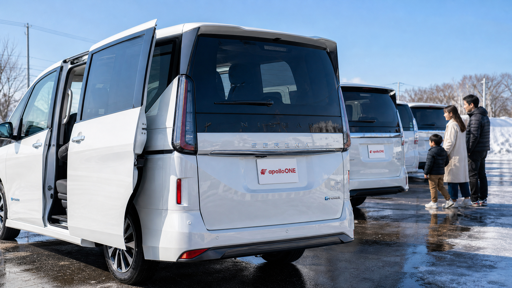 晴れた冬の屋外展示場に並べられた白いミニバンの様子。手前の車はスライドドアが開いて広々とした室内空間が見え、奥には在庫車を見て回る家族連れが写っている。