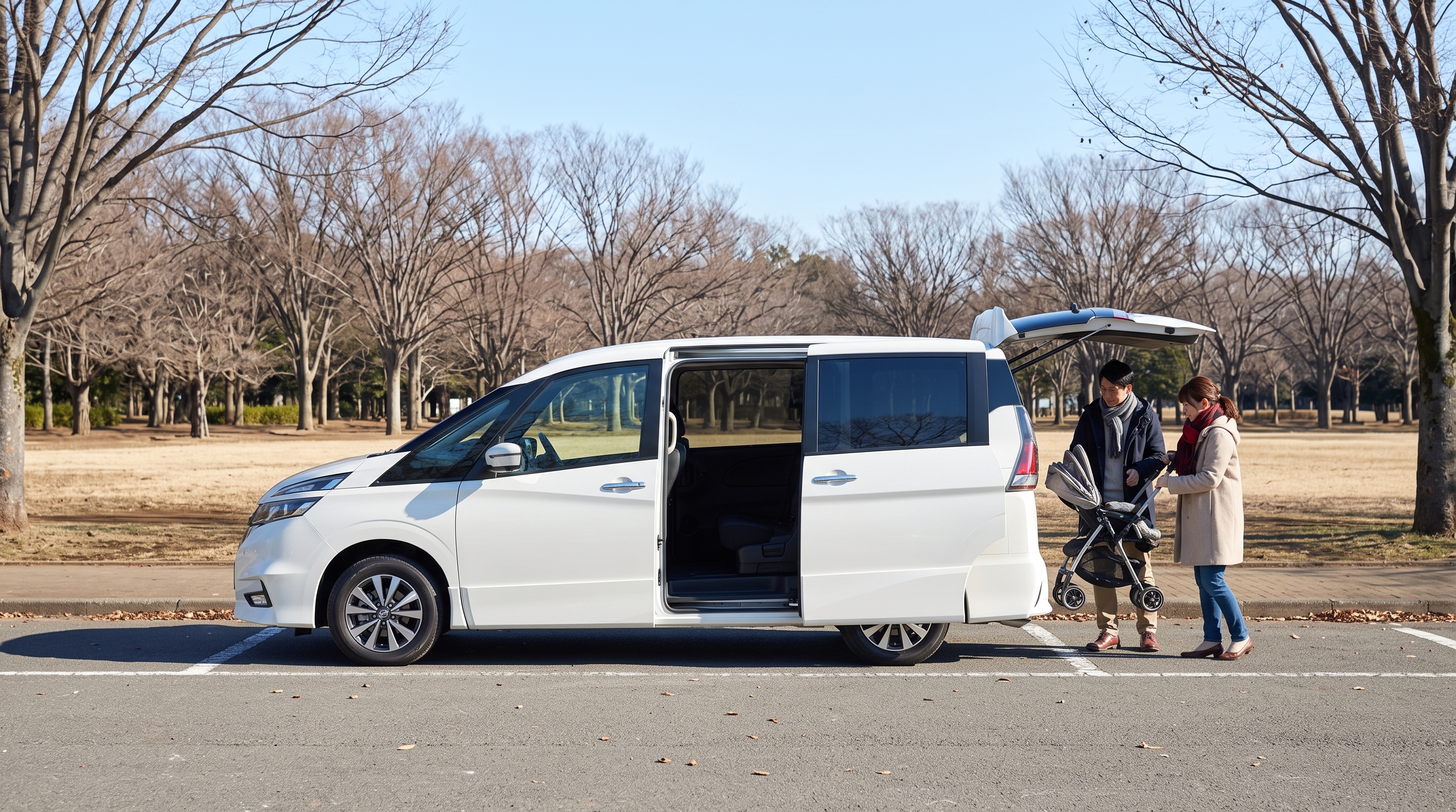 冬の公園横の駐車スペースに停められた白いミニバンの様子。スライドドアを大きく開け、夫婦が広々とした後部座席にベビーカーを積み込んでいるシーン。