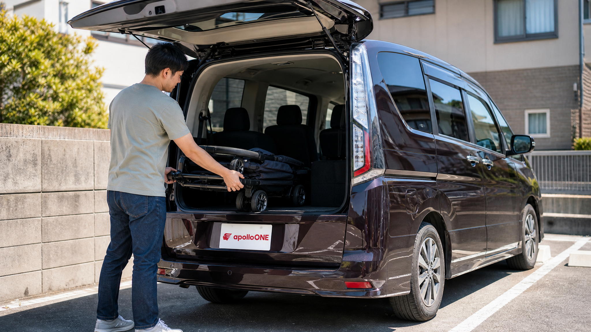 夏の強い日差しの中、ミニバンのリアハッチの上半分だけを開けて、狭い駐車スペースでベビーカーを積み込もうとしている父親の姿。使い勝手の良さが伝わる日常のシーン。