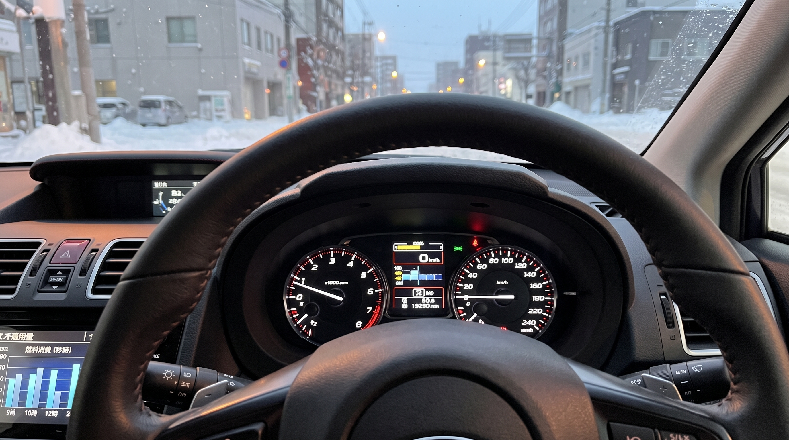 雪が積もった冬の市街地を窓の外に望む、運転席のメーターパネルとステアリング周りのクローズアップ。ディスプレイには燃費推移を示すバーグラフが光っている様子。