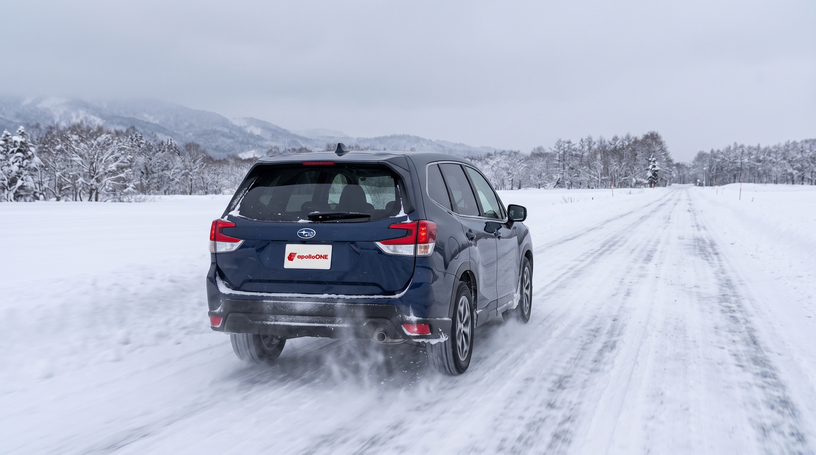 冬の曇り空の下、雪に覆われた直線道路を安定して走行する四輪駆動車の後ろ姿。路面から雪煙が巻き上がり、雪道での力強い走りと過酷な冬の環境を感じさせる様子です。