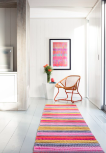 Pink and orange striped runner rug with a brown chair and pink wall art