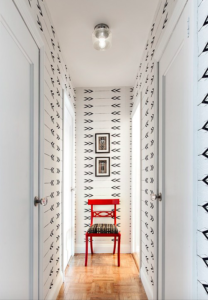Red chair at the end of a long hallway with white and black wallpaper