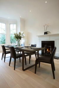 Black dining chairs around a rectangular brown table with white fireplace mantle and light wood floors