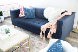 blue tufted sofa with throw pillows and two throws