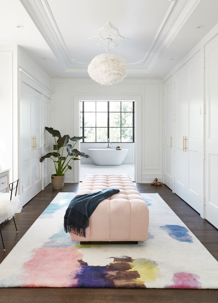 long room with huge pink tufted ottoman on abstract colored rug