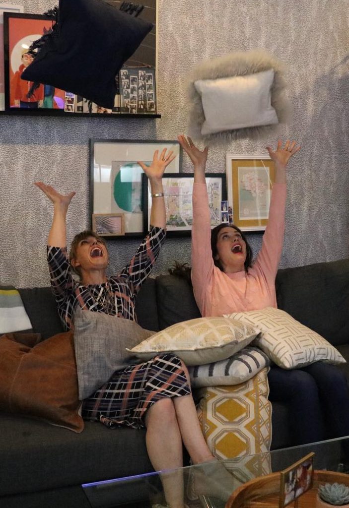 two women with arms in the air sitting on black sofa