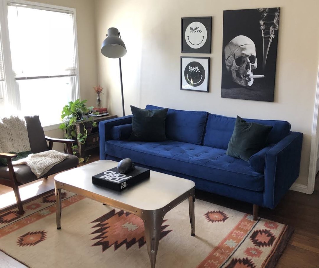 blue sofa with tufting on seat and skull smoking picture on wall