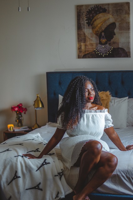 Woman in a white dress sitting on a bed with a blue tufted headboard and Eiffel Tower sheets