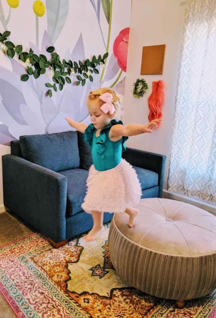 young girl climbing on pink ottoman