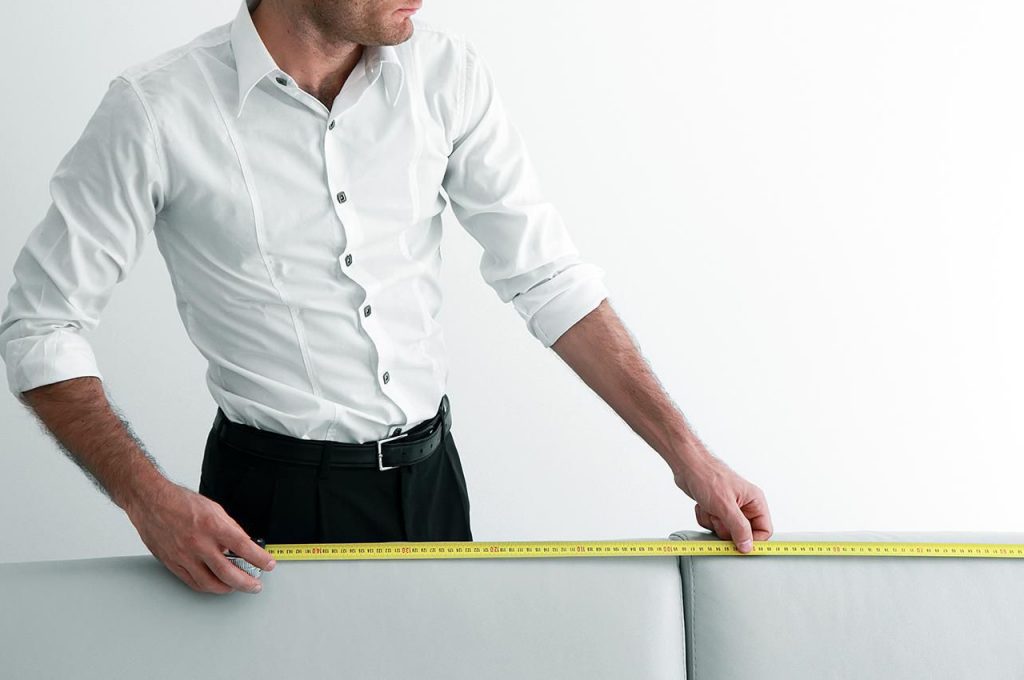 man measuring a grey sofa with measuring tape