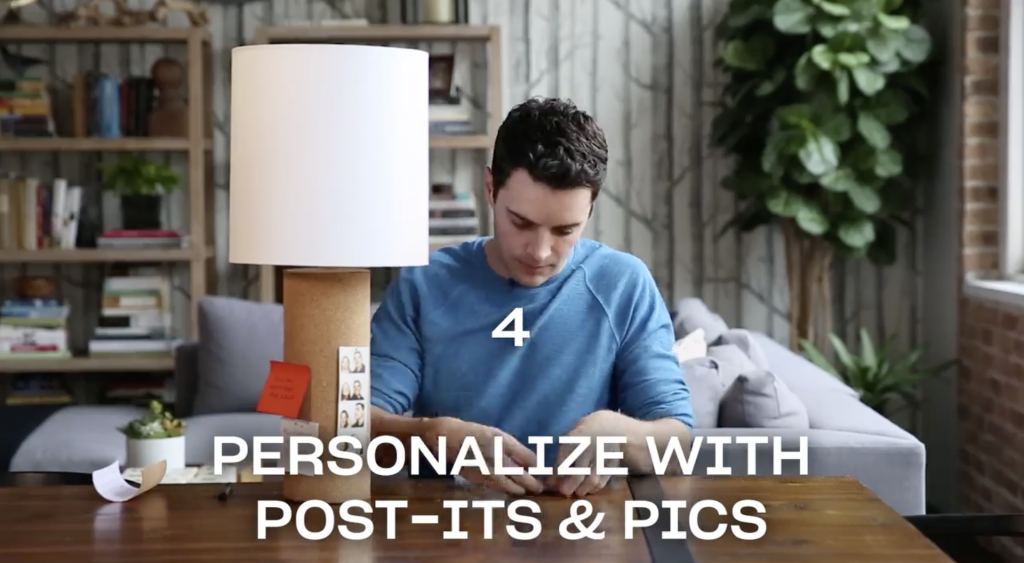 Man decorating a table lamp with photos attached to cork on the lamp base