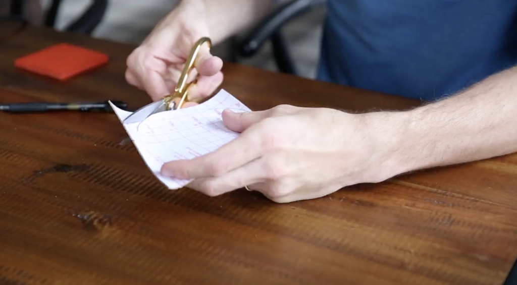 Man cutting paper with gold scissors at a brown wooden table
