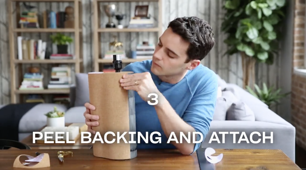 Man attaching cork paper to a table lamp base while seated