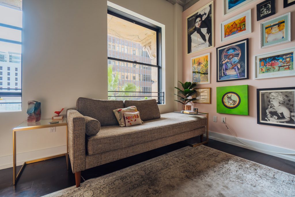 room with grey couch, pillows, side table, paintings, a plant and rug