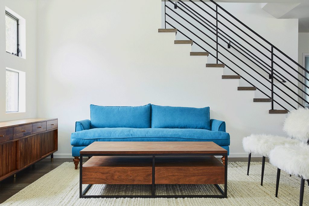 empty white room with a staircase, blue sofa, wooden coffee table and beige rug