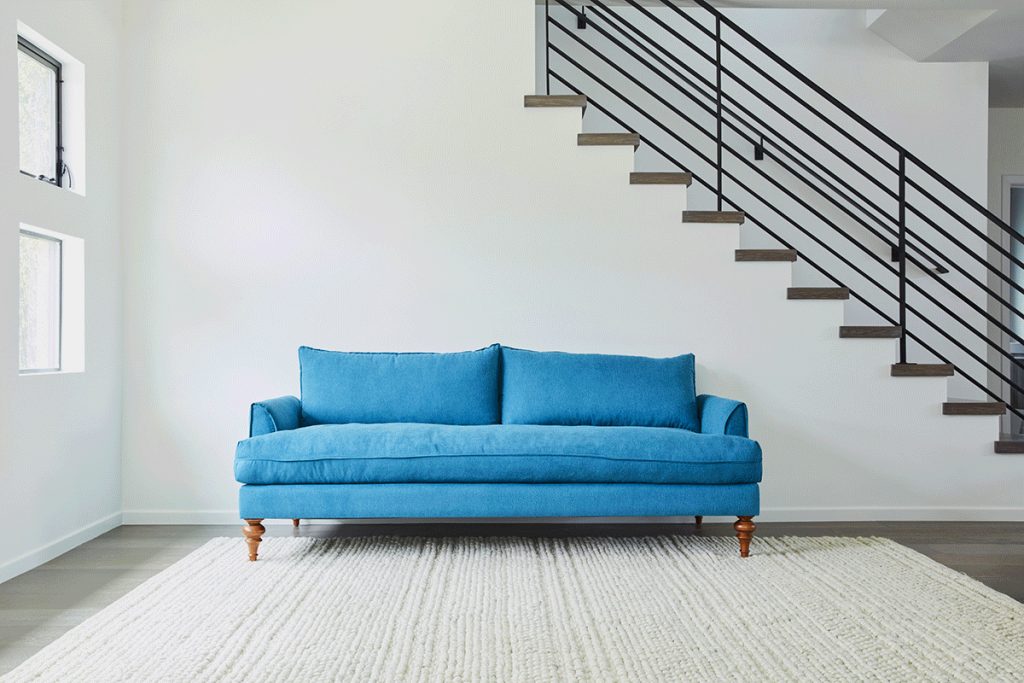 empty white room with a staircase, blue sofa and beige rug
