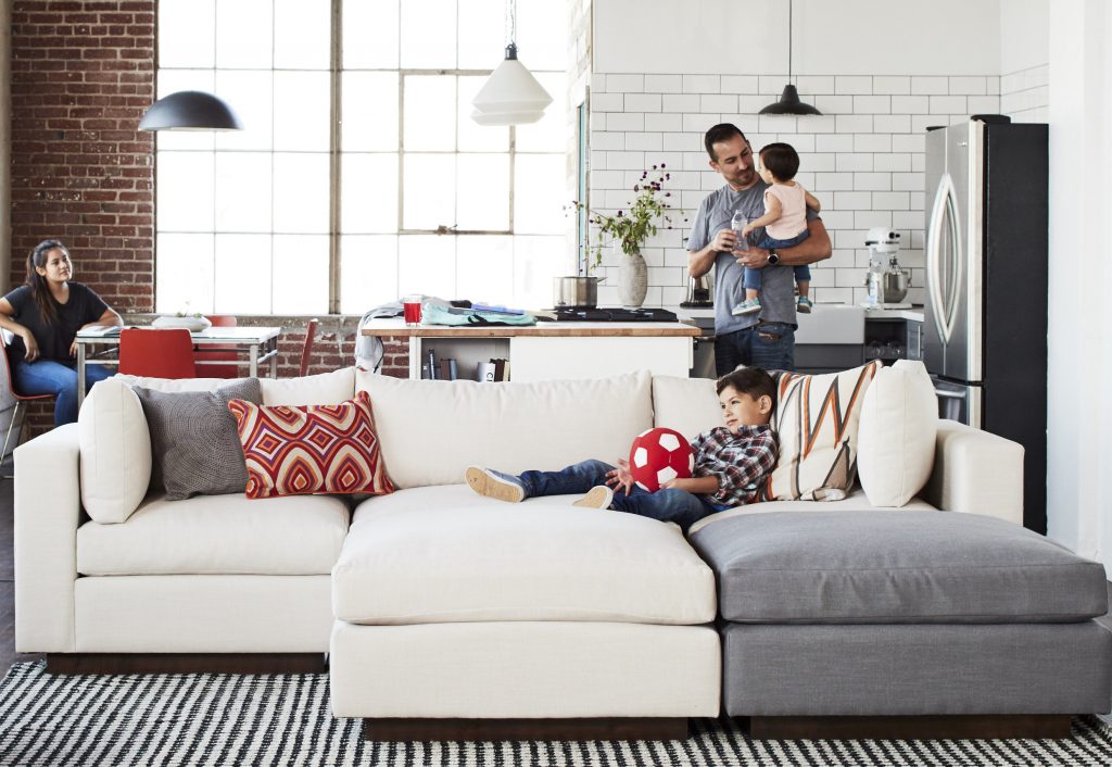 room with woman, child on sofa, man standing holding a baby 