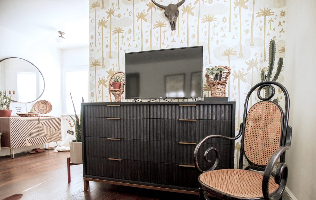 brown media storage next to a brown chair, tv and wall art