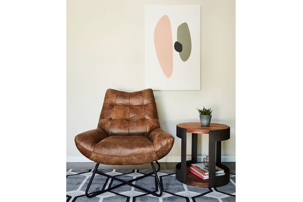 brown chair next to a wooden side table and painting all on a rug