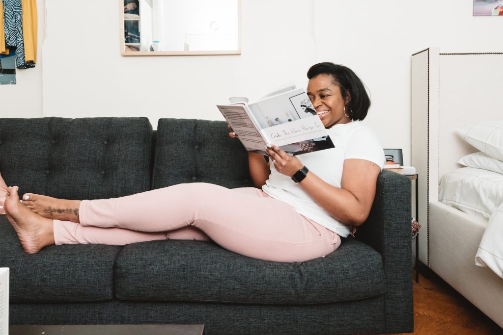 woman laying on black sofa with a book