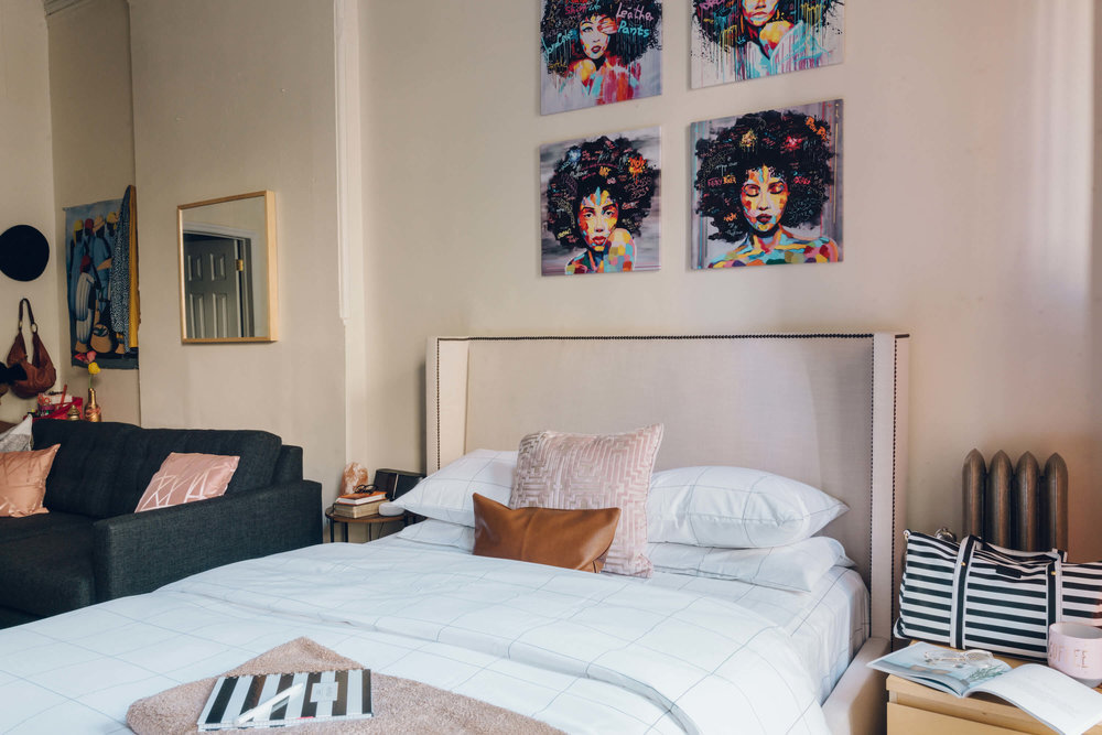 room with white bed, paintings, black sofa, mirror and side table