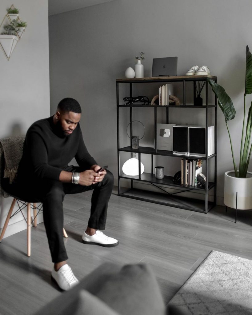 man sitting in a chair in a room with a book shelf, rug and plant