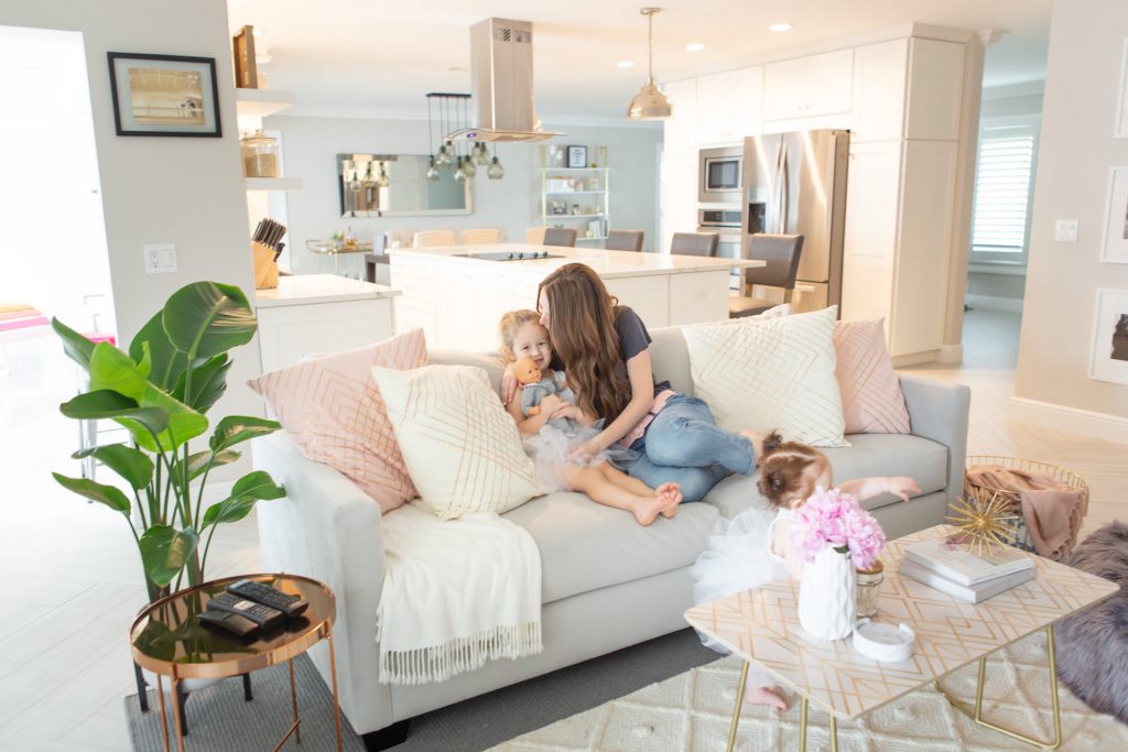 woman and young girl sitting on grey sofa with another young girl on white rug