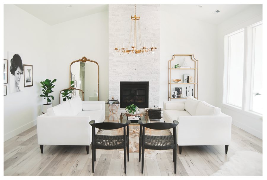 white sofas, two black chairs surrounding a fireplace, table with a plant, mirror, book shelf, paintings and plant