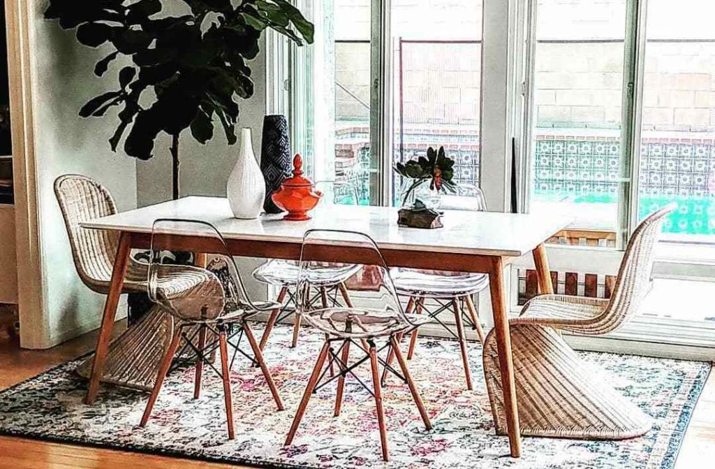 wooden dining table with four clear chairs and two wooden chairs on a multicolored rug with plants and vases