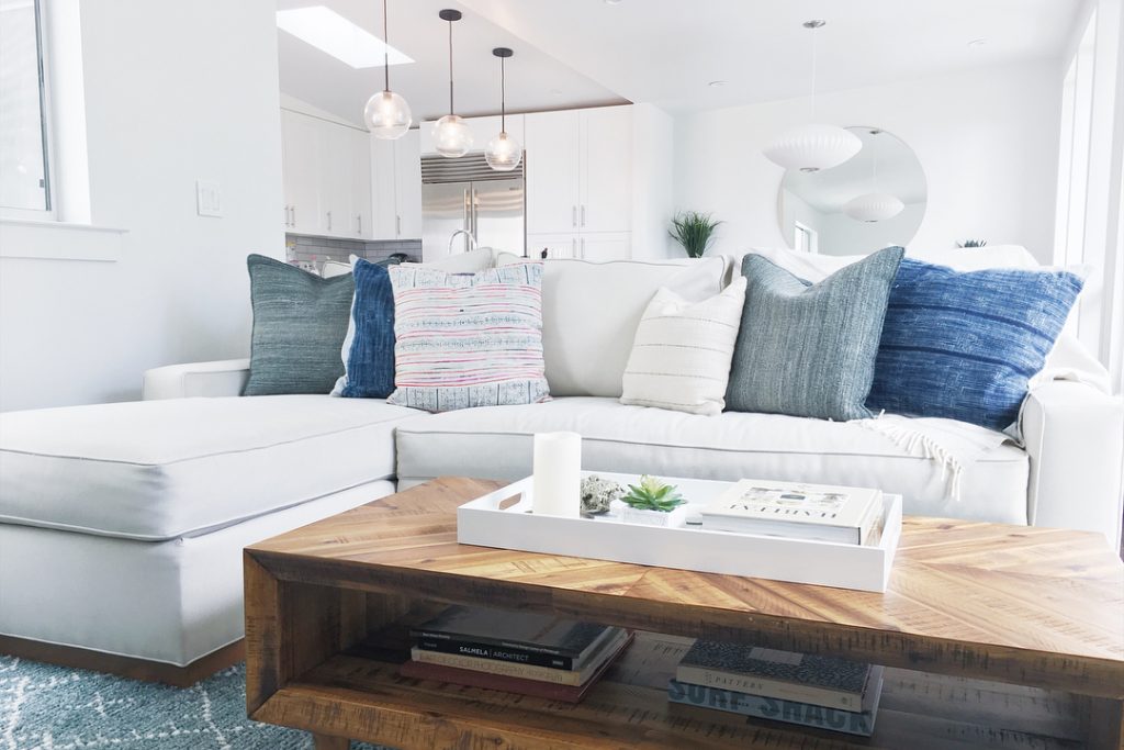 white sofa with a variety of pillows, wooden coffee table with book, plant and candle