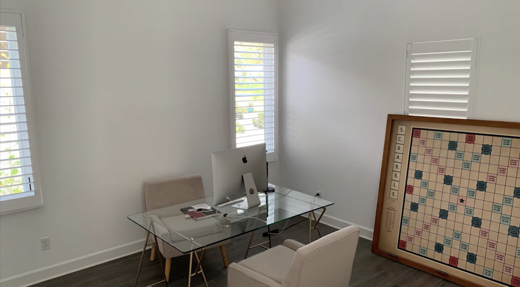 room with a laptop on a glass desk, two beige chairs and a large game board