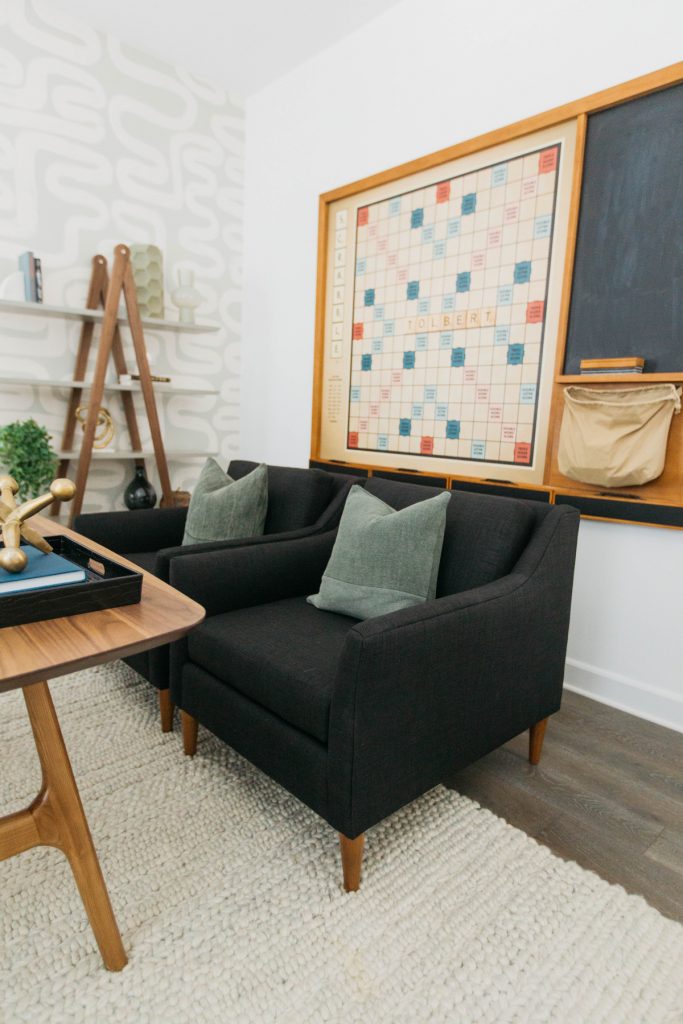 two black chairs with green pillows, a wooden desk, a beige rug and a large gaming board