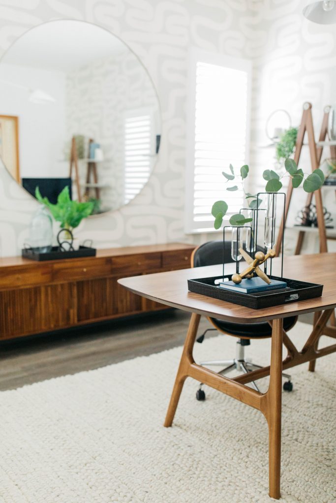 desk with desk art, wooden console, mirror, plant and a beige rug