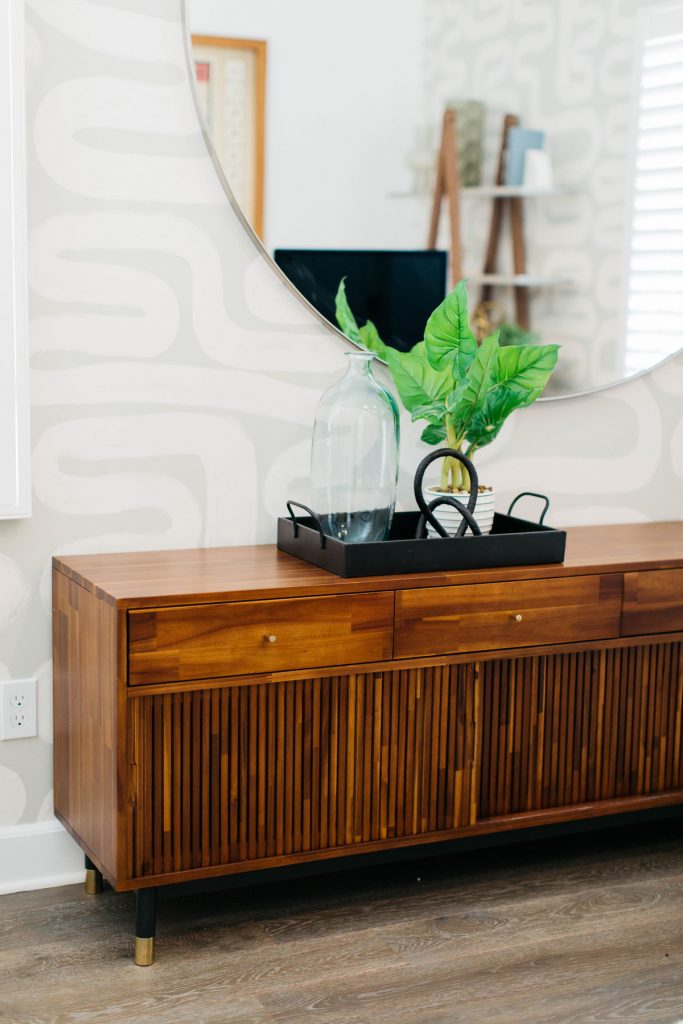 wooden console with a black tray on it, a plant and vase surrounded by a mirror