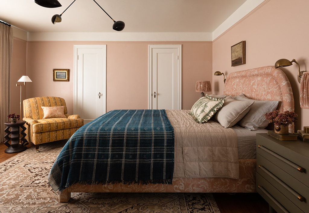 pink bed with green blanket on top of a beige rug next to a yellow chair and lamp