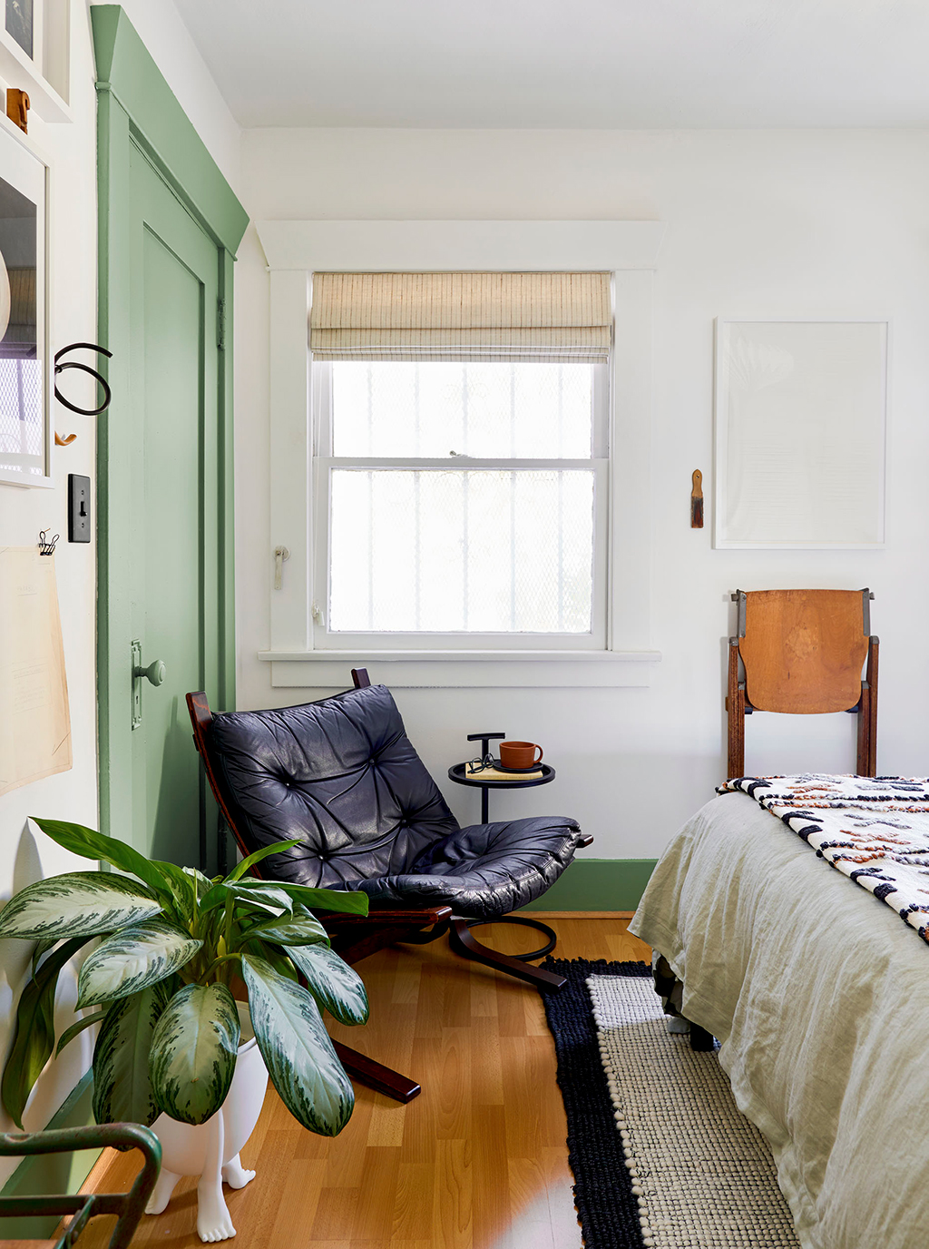 room with green and white walls with a black leather chair, bed and plant in it