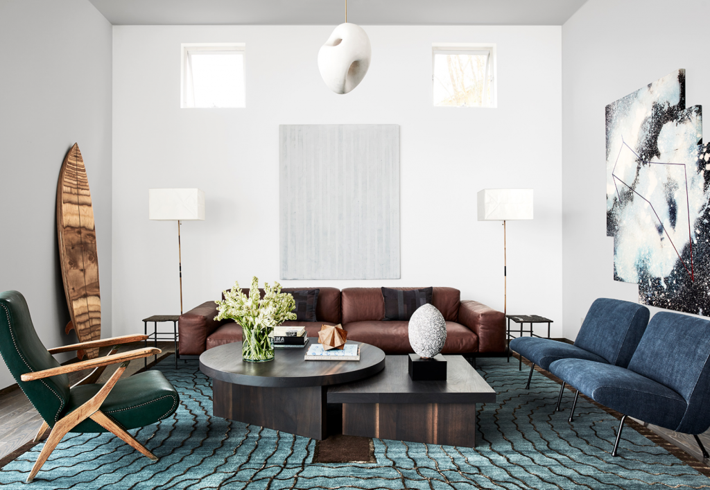 room with brown sofa, large brown coffee table, surf board, lamp and blue chairs