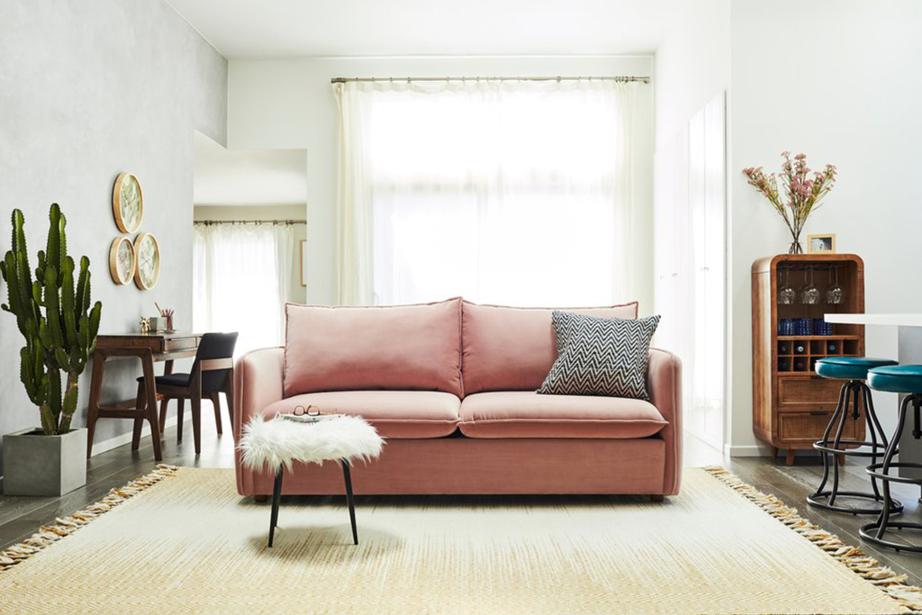 blush velvet sofa with a pillow on it next to a white ottoman, cactus, chair, desk, paintings, wine cabinet, white counter and chairs