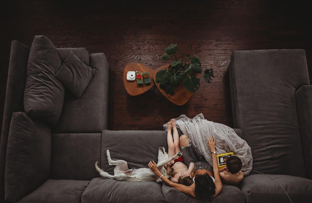 grey sofa with three people and a dog sitting on it beside a wooden coffee table