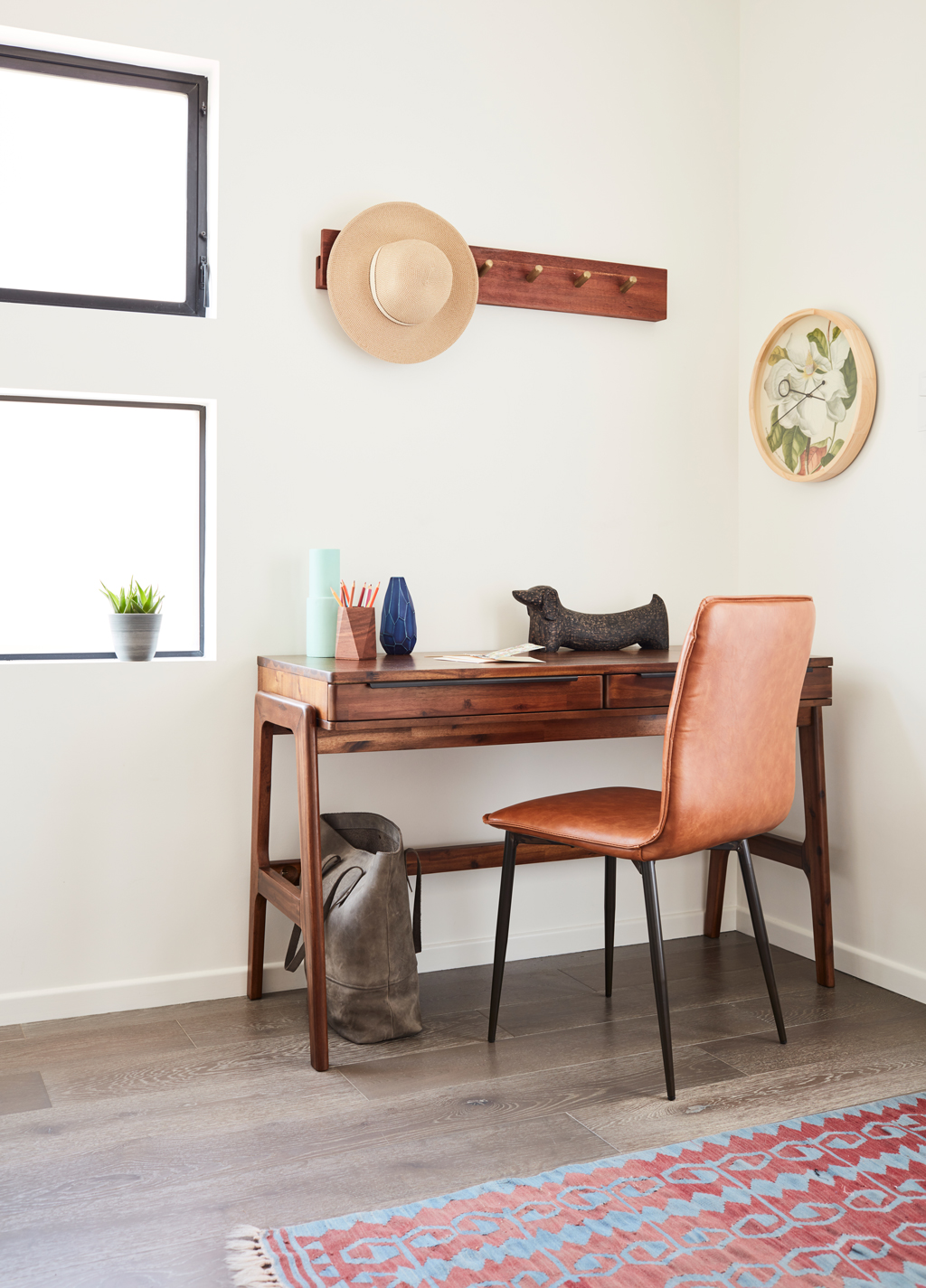 wooden desk with brown chair beside a clock, bag, rug and hat stand