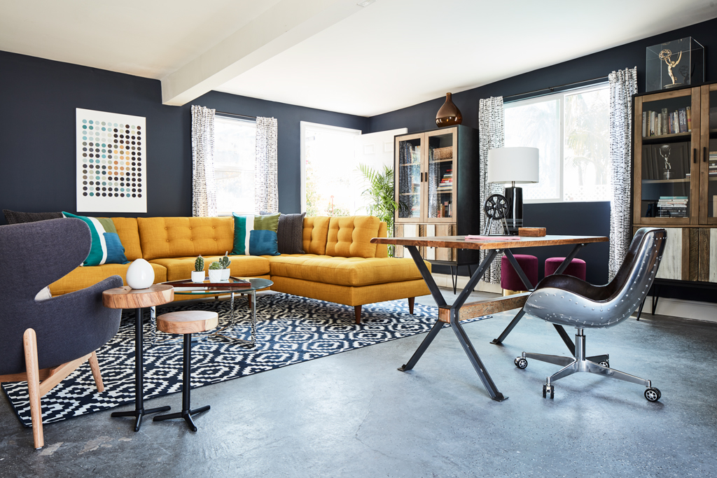 room with a yellow sofa, brown desk, desk chair, lamp, cabinet, book shelf, rug, two side tables and a grey chair