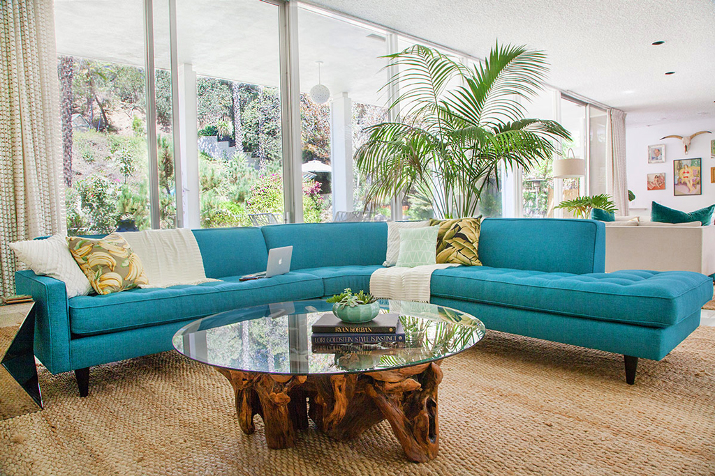 blue sofa with pillows, blankets and a laptop on it beside a clear and wooden table