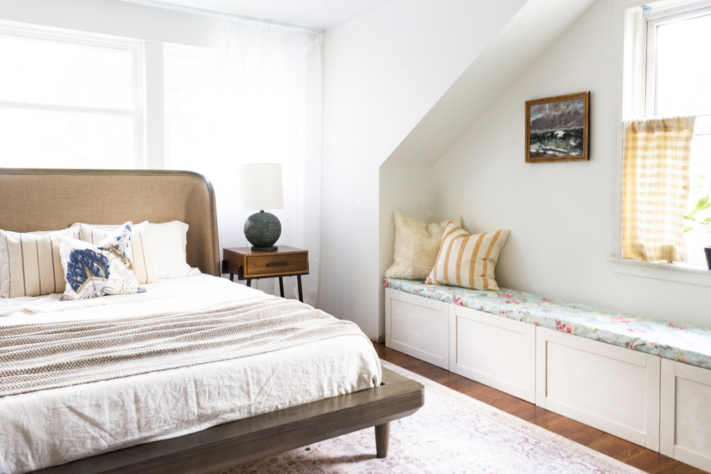 brown bed with a white cover and pillows next to a white wall bench