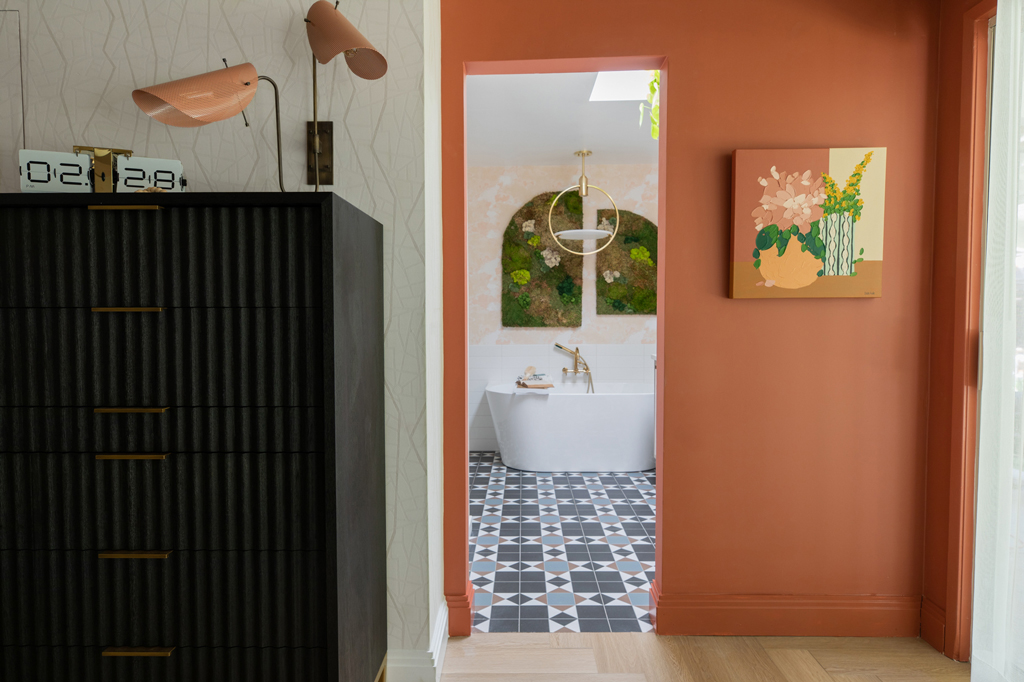 orange and white wall papered room with a black dresser, lamp, clock, bathtub and painting