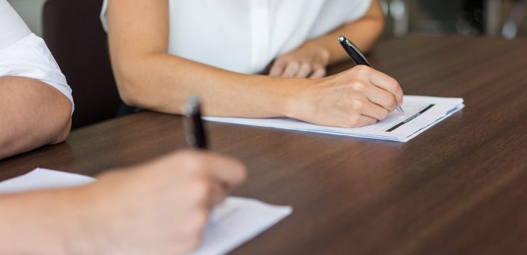 Imagen de dos brazos de personas escribiendo en un papel sobre una mesa