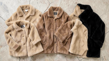 Multiple genuine sheepskin shearling coats in tan, brown, and black displayed flat on a neutral surface showing wool interiors and leather exteriors
