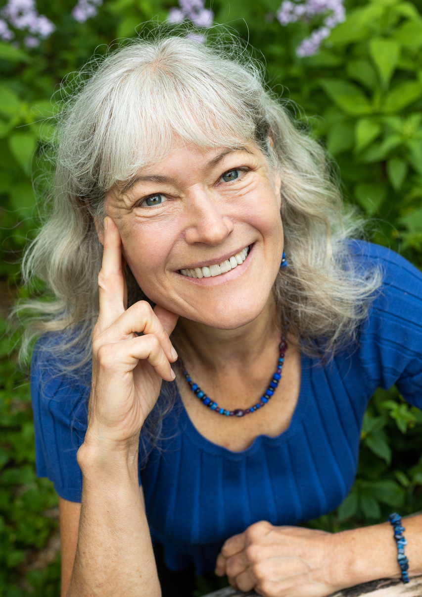 Kathleen Rude smiling in front of a garden, wearing a blue knit top