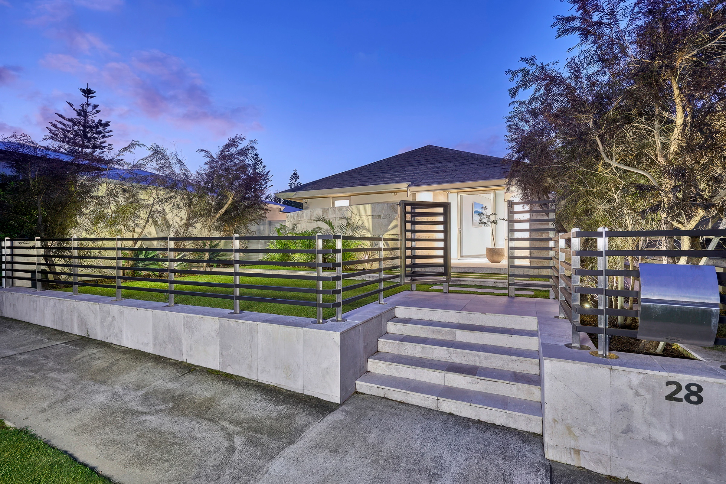 Contemporary house surrounded by trees and a metal railing fence at twilight